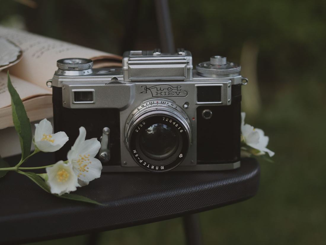Aparat fotograficzny z obiektywem na stole obok białych kwiatów